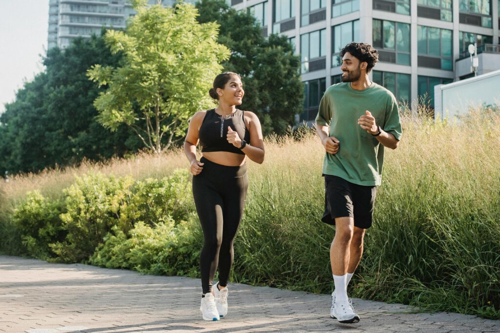 Fit couple jogging together in a sunny city park, embracing an active lifestyle.