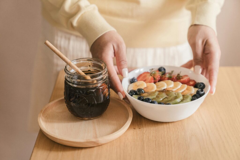 A person arranging a healthy fruit bowl with syrup on a wooden table.